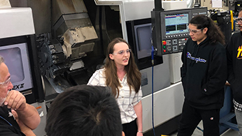 A woman talking to a group in front of a CNC machine.